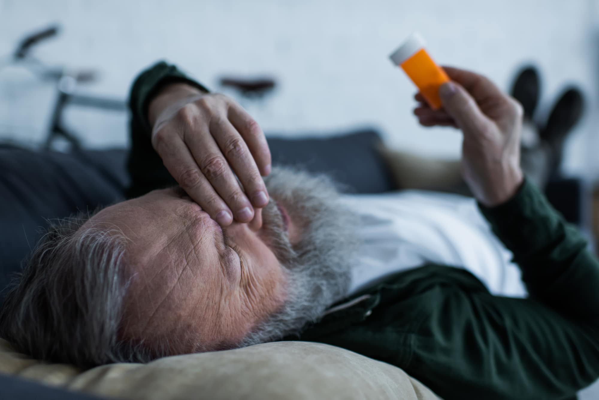 Man on couch looking distressed holding an empty pill bottle
