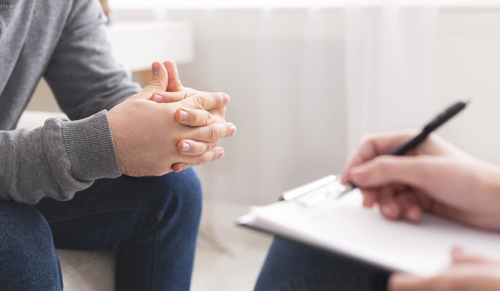 Therapist writing notes during a Cognitive Behavioural Therapy session with male sitting on the couch