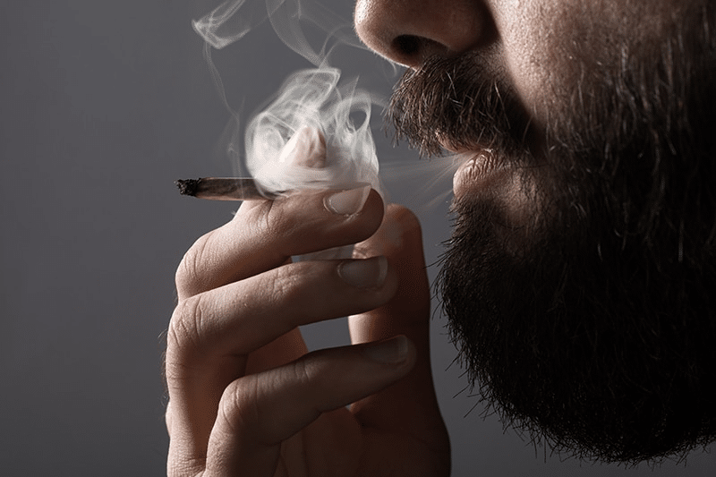 a close up of a man smoking a marijuana cigarette