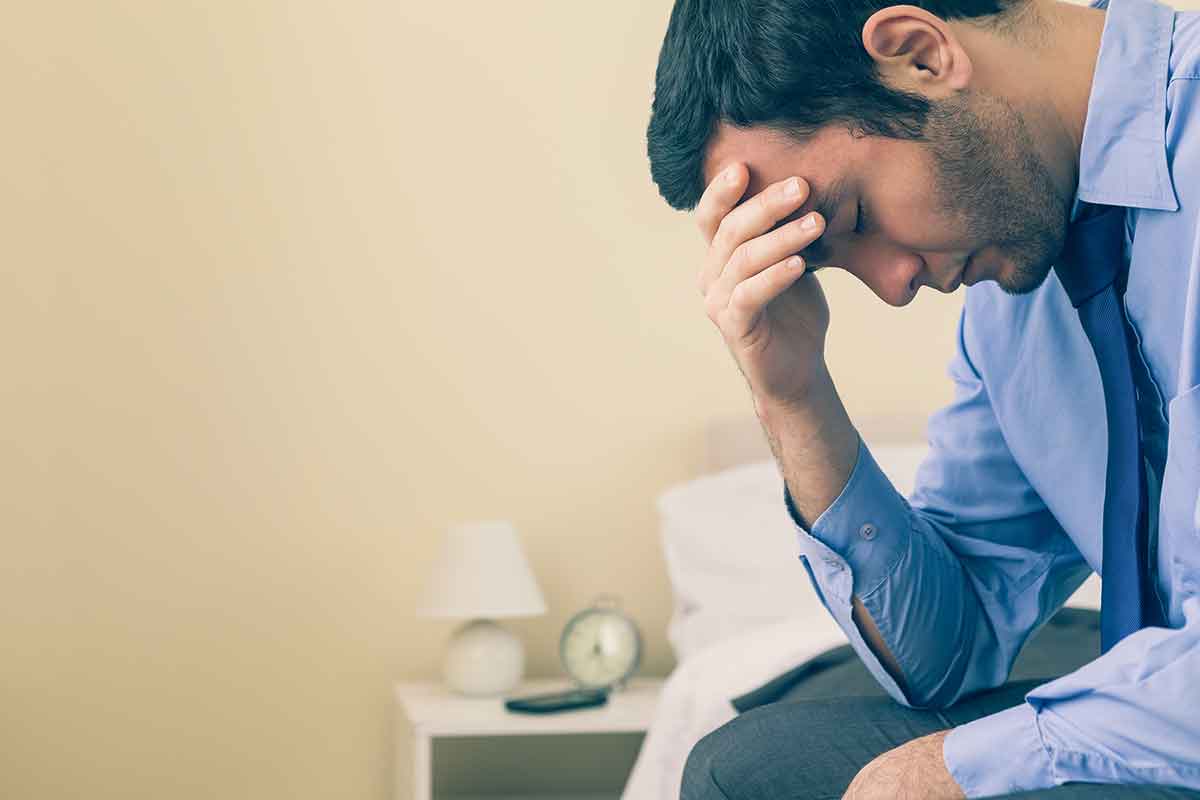 a man sitting on a bed with his head in his hand